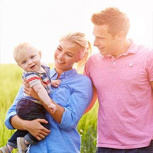 young family of three smiling together in a field